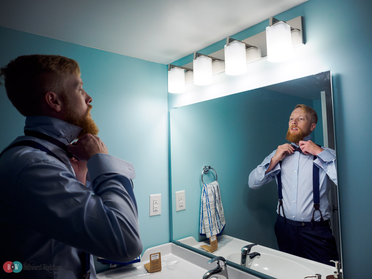 Groom tying tie in bathroom mirror