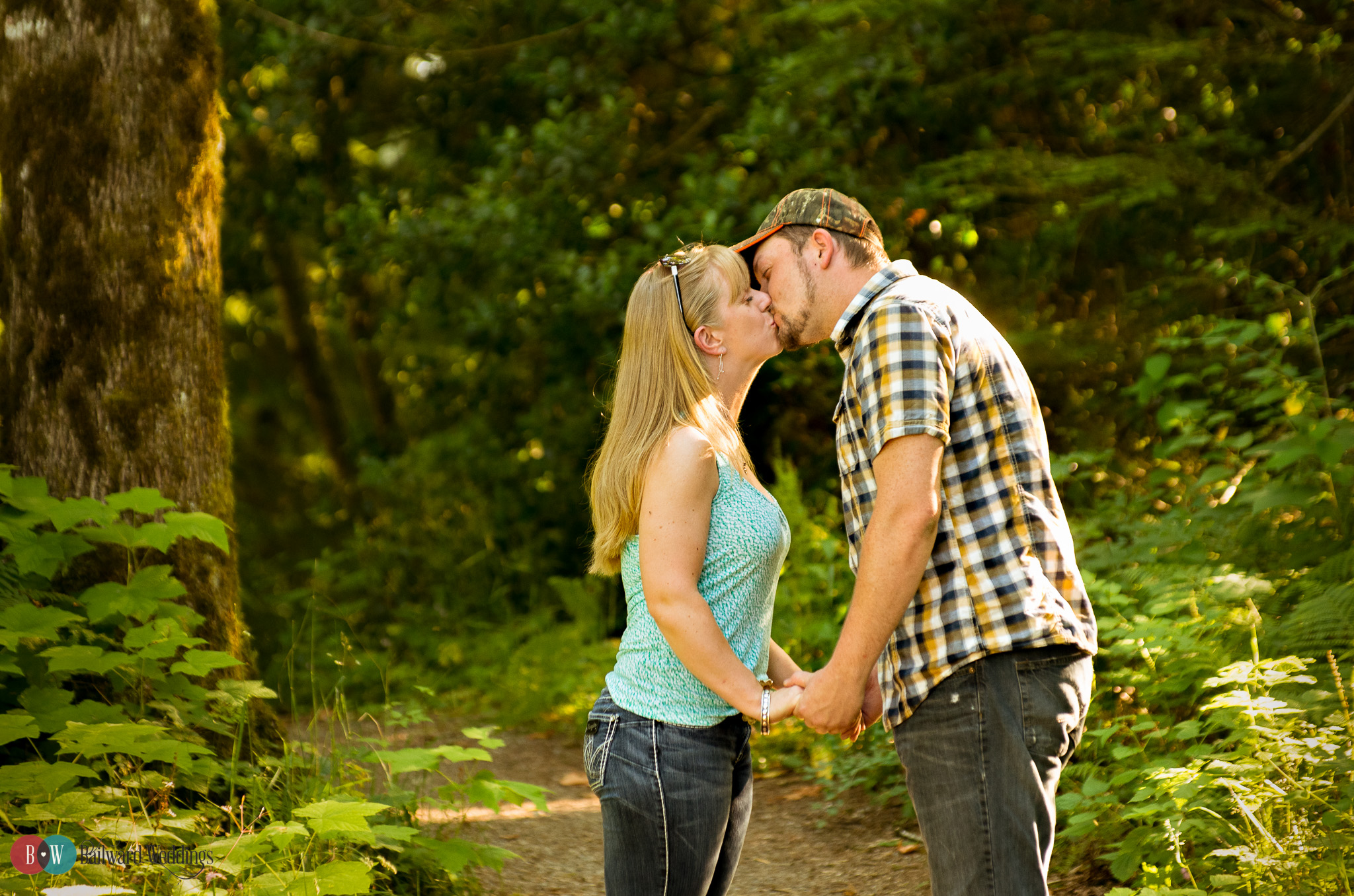 Engaged couple kissing on trail in trees